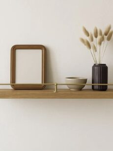 Barre de galerie en laiton massif sécurisant un cadre déco et un vase sur une étagère en chêne.