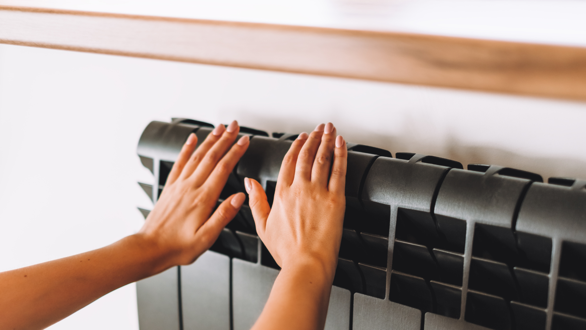 Personne qui se réchauffe les mains près d'un radiateur muni d'une tablette en bois